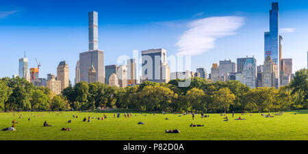 People relax on the grass away from the hustle and bustle of the city beyond, in Strawberry Fields, part of Central Park in New York Stock Photo