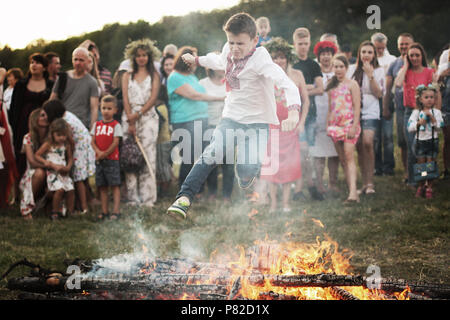 KYIV, UKRAINE - JULY 6, 2018: Young boy jumps over the flames of bonfire during the traditional Slavic celebration of Ivana Kupala holiday in Pirogovo Stock Photo