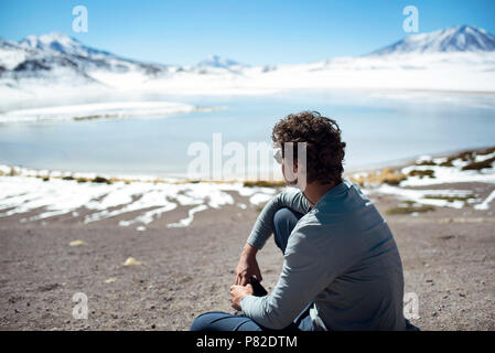 Rear view of boy looking at the snowy view of a lagoon within Eduardo Avaroa Andean Fauna National Reserve, Bolivia. Jun 2018 Stock Photo