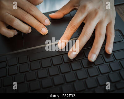 Close-up hands touching pad on computer laptop keyboard on wooden table background Stock Photo