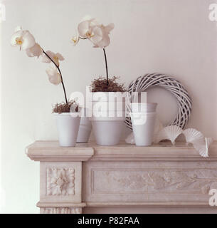White orchids in white painted flower pots on marble mantelpiece with a painted woven wreath Stock Photo