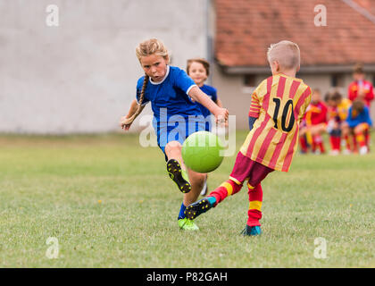 Kids soccer football - young little girl is shooting ball at soccer field Stock Photo