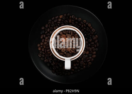 White cup full of coffee beans on black plate filled with roasted coffee beans. With negative space on black background. Stock Photo