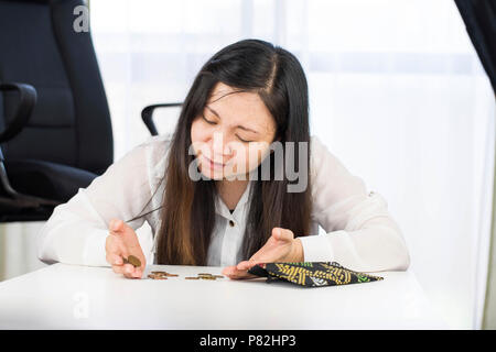 A bankrupt, broke and frustrated woman is having financial problems with coins left on the table and an empty wallet. Stock Photo