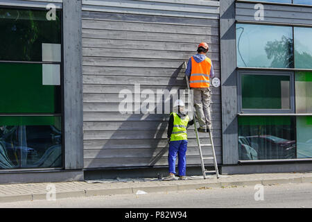 two workers dressed in a safety vest and helmets painting the wall Stock Photo