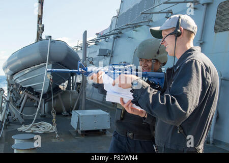 SOUTH CHINA SEA (July 25, 2016) – Fire Controlman 2nd Class Ethan Larsen, a member of the anti-terrorism training team, right, observes Boatswain’s Mate Seaman Precious Aumua, left, aim her training weapon at a simulated attacking swimmer during anti-terrorism force protection drills aboard the Arleigh Burke-class guided-missile destroyer USS Curtis Wilbur (DDG 54). Curtis Wilbur is on patrol with Carrier Strike Group (CSG) 5 in the U.S. 7th Fleet area of responsibility supporting security and stability in the Indo-Asia-Pacific. Stock Photo