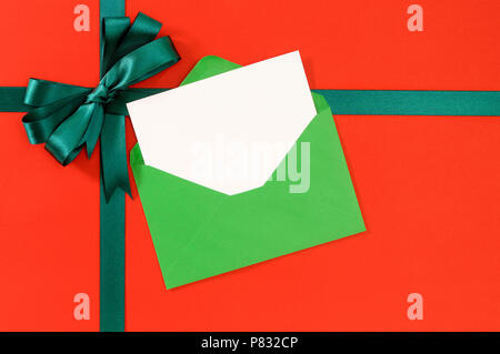 Christmas or birthday card on red gift paper background with green ribbon bow. Stock Photo