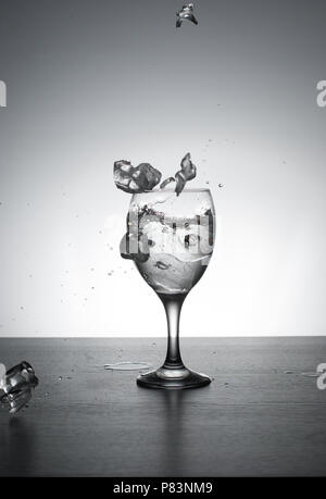 Water being poured into wine glass, backlit on white background with splashes.Fast shutter. Frozen motion. Stock Photo