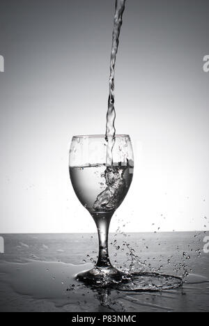 Water being poured into wine glass, backlit on white background with splashes.Fast shutter. Frozen motion. Stock Photo