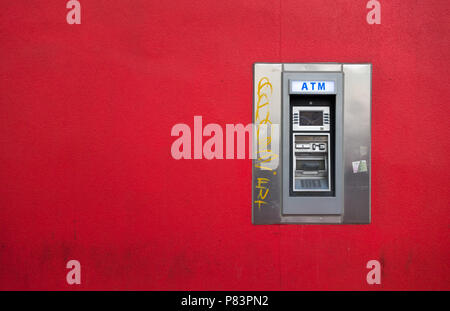 An automated teller machine (ATM) is a stark contrast on the bright red wall where it is mounted.  Toronto, Ontario, Canada Stock Photo