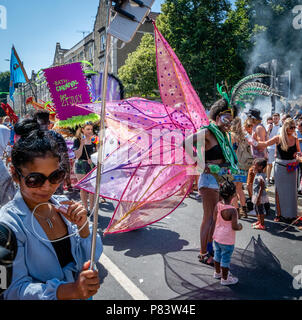 Woman with smartphone camera and selfie stick photographing colourful flamboyant costumes at St Paul's carnival in Bristol UK Stock Photo