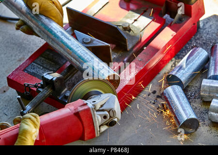 A construction worker using a grinder on a newly cut galvanized steel pipe Stock Photo