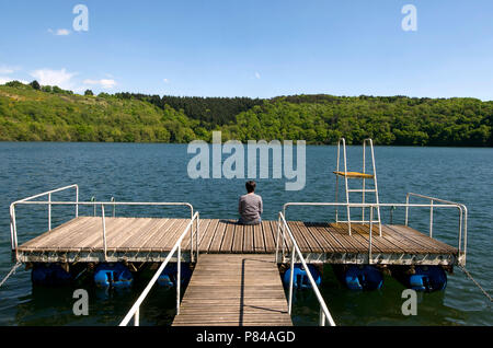 Woman sitting on a pontoon looking out over a lake, Auvergne, France Stock Photo