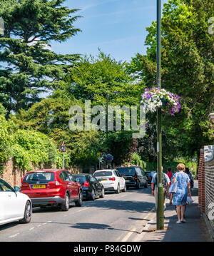 Hanging flower baskets in Wimbledon colours of purple and white with people walking & car traffic jam during tennis championship, London, England, UK Stock Photo