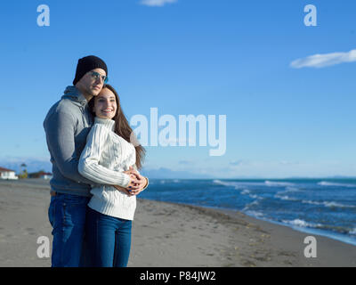 Young couple having fun walking and hugging on beach during autumn sunny day Stock Photo