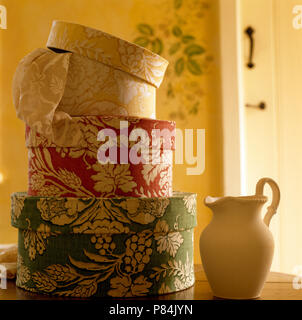 Close-up of three hat boxes covered in foliage patterned fabric on table with a cream pottery jug Stock Photo