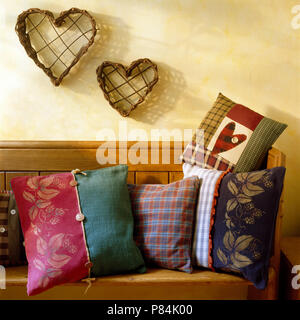 Heart shaped twig ornaments on wall above an old pine settle with cushions stenciled with a grapes pattern Stock Photo