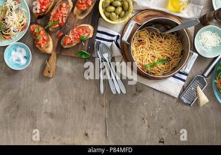 Italian dinner table with pasta and bruschetta on light rustic wooden table, top view