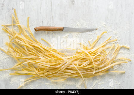 Raw homemade noodles with knife on a white background, top view Stock Photo