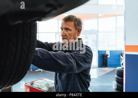 Mechanic fastening the wheel of a car in service station. Man replacing wheel of a vehicle lifted in garage. Stock Photo