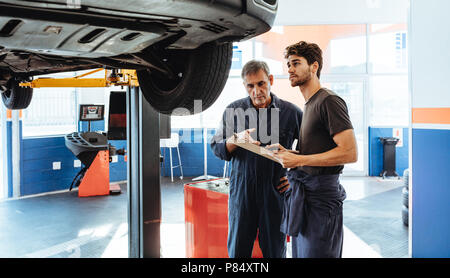 Two car mechanics making a list on clipboard while examining the car. Mechanics making list of repairs on a car in auto service station. Stock Photo