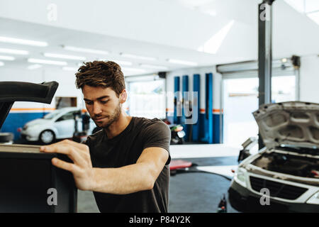 Young mechanic doing car check up on computer. Mechanic using computerized equipment to diagnose a car in service station. Stock Photo