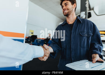 Young auto mechanic shaking hands with satisfied customer in garage. Automobile service center worker shaking hands with client after car servicing. Stock Photo