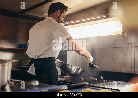 Male cook making some food in a food truck parked under a tree. Man chopping vegetable on his food truck. Stock Photo