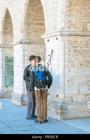 TALLINN, ESTONIA - MAY 1, 2011: Two young men look at metal collar and ring for hands and feet on the small pillory on the City Hall wall. Stock Photo