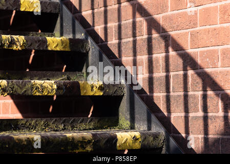 Close-up of steps painted with black and yellow hazard stripes. Verticalstriped shadow cast by handrail on wall Stock Photo