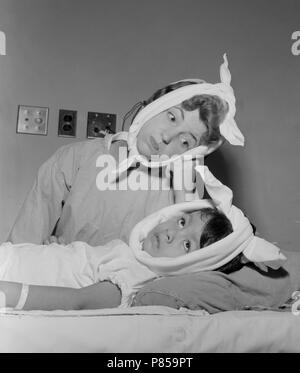A nurse comiserates with her patient with the mumps, ca. 1960. Stock Photo