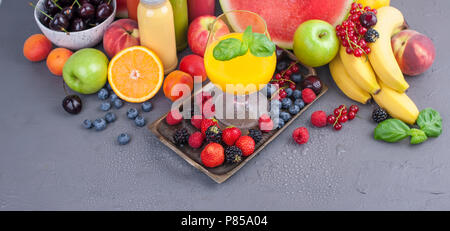 Juice in bottles, different and in a glass. Assorted berries and fruits. Gray background. Detox food. Copy space Stock Photo