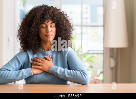 African american woman at home smiling with hands on chest with closed eyes and grateful gesture on face. Health concept. Stock Photo