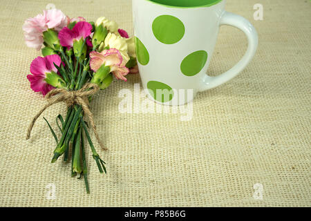 carnation bouquet tied with string and polka dot mug on burlap Stock Photo
