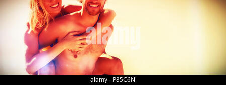Portrait of young man piggybacking beautiful woman at beach Stock Photo