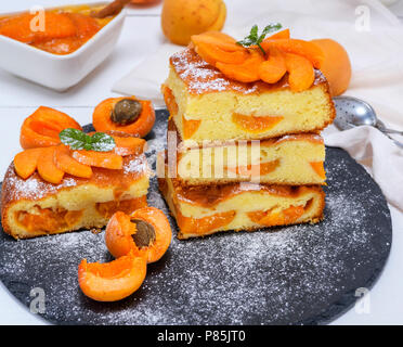 square pieces of apricot pie on a black graphite plate, sponge cake sprinkled with powdered sugar, top view Stock Photo