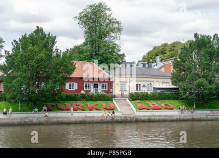 TURKU, FINLAND - 8/7/2018: Sign of Turku written by flowers in Finnish and Swedish by the Aura river and Pharmacy museum in the old wooden building Stock Photo