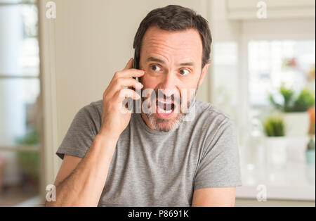 Middle age man using smartphone scared in shock with a surprise face, afraid and excited with fear expression Stock Photo