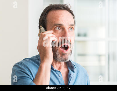 Middle age man using smartphone scared in shock with a surprise face, afraid and excited with fear expression Stock Photo