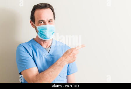 Senior doctor man using mask very happy pointing with hand and finger to the side Stock Photo