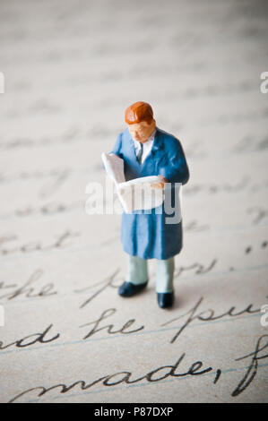 miniature figurine of a man reading a newspaper and standing on a handwritten letter