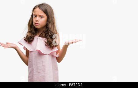 Brunette hispanic girl wearing pink dress clueless and confused expression with arms and hands raised. Doubt concept. Stock Photo