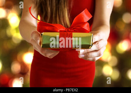 Hands giving gold paper wrapped gift box with red ribbon as a present for Christmas Stock Photo