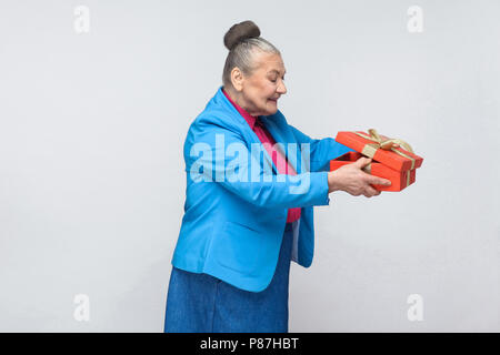 Cunning aged happy woman unboxing looking inside the gift box. emotional expressive grandmother in blue suit with collected gray hair bun hairstyle. i Stock Photo