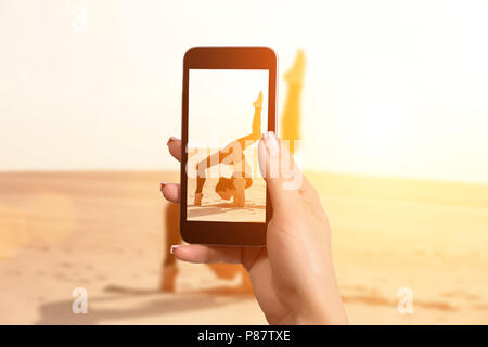 Woman taking a picture with your mobile phone a one woman doing acrobatic stunt on sand Stock Photo