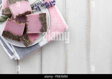 Handmade lavender soap, bath towel and flower blossoms on white wooden background. Natural cosmetics concept. Stock Photo