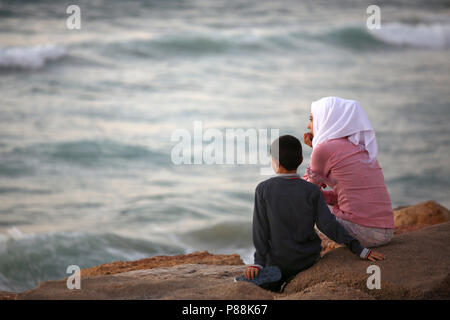 Young Muslim Israeli woman and son looking out to sea at dusk Stock Photo