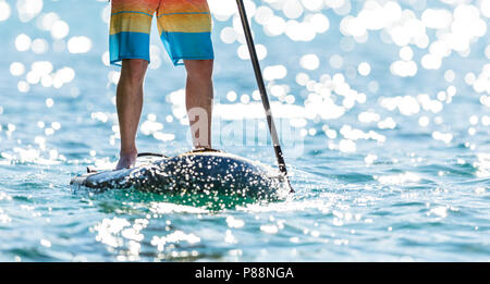 Man standing on paddle board, on water, at sunset, holding fishing rod  stock photo