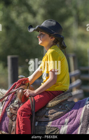 Young, smiling, male with cowboy hat, sitting tall in saddle, looking straight ahead. Side angle shot. Model Release #105. Stock Photo