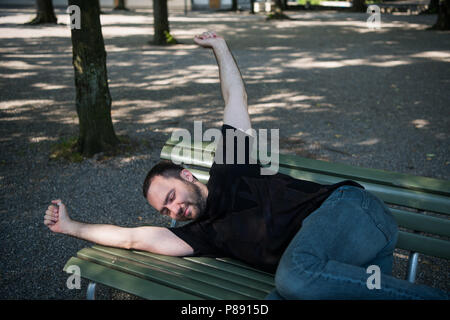Young man lying down sleep on bench in the park and wakes up after rest Stock Photo